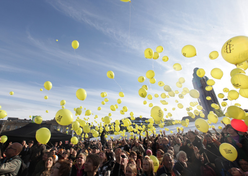 Yellow balloons in the sky above a crowd of people.