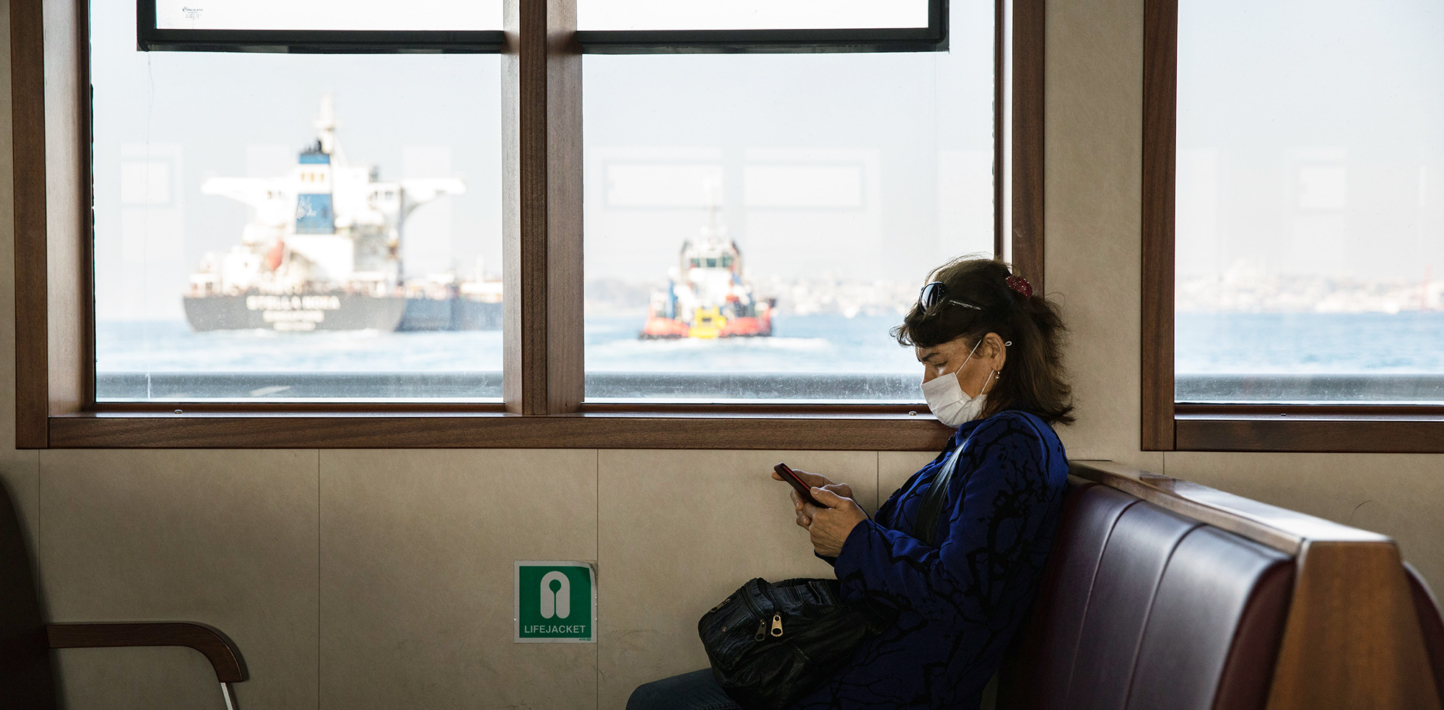A woman checking her phone, wearing a protective face mask against COVID-19 infection - travelling on an empty public ferry Istanbul, Turkey, April 27, 2020.