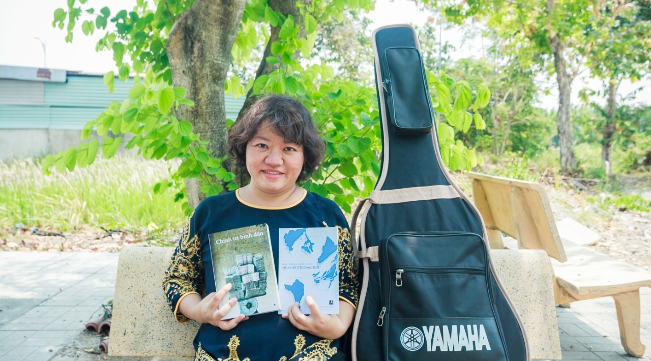 A portrait of Pham Doan Trang, posing with books and her guitar.