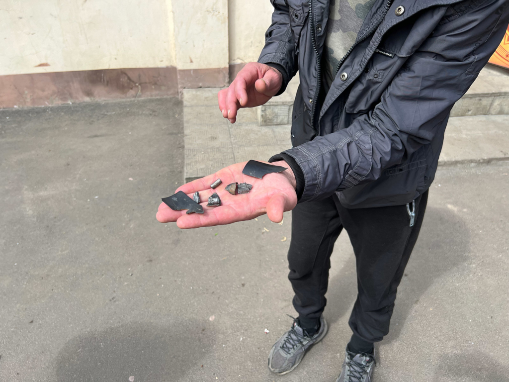 Sasha showing fragments of cluster munitions which exploded near his shop; the fragments killed a man nearby and flew into the store.