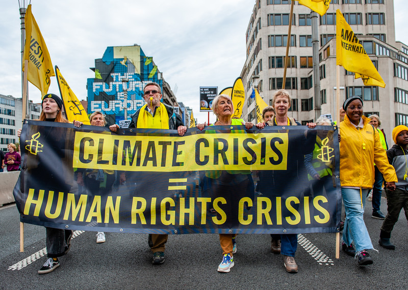 Protesters wearing yellow hold a large banner with the words: "climate crisis = human rights crisis". 