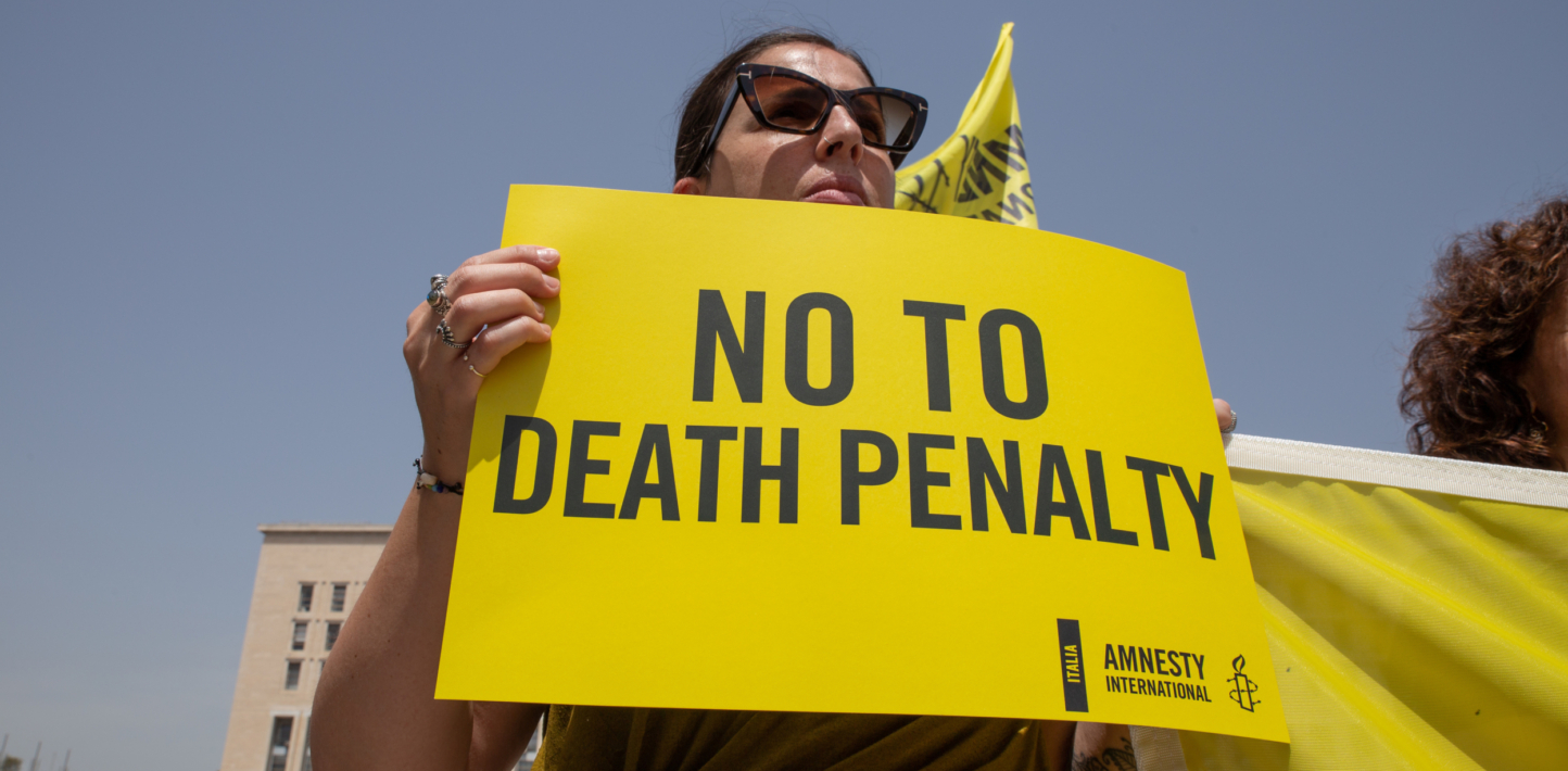 Activist holding yellow Amnesty International logo-ed placard with writing: "No to Death Penalty."