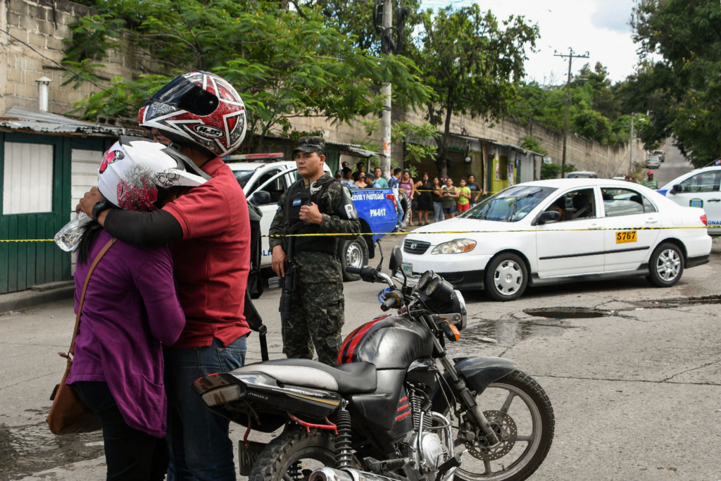 two people embrace after a loved one was shot dead. They appear to have arrived at the scene of the crime on motorbike and are still wearing their helmets. 