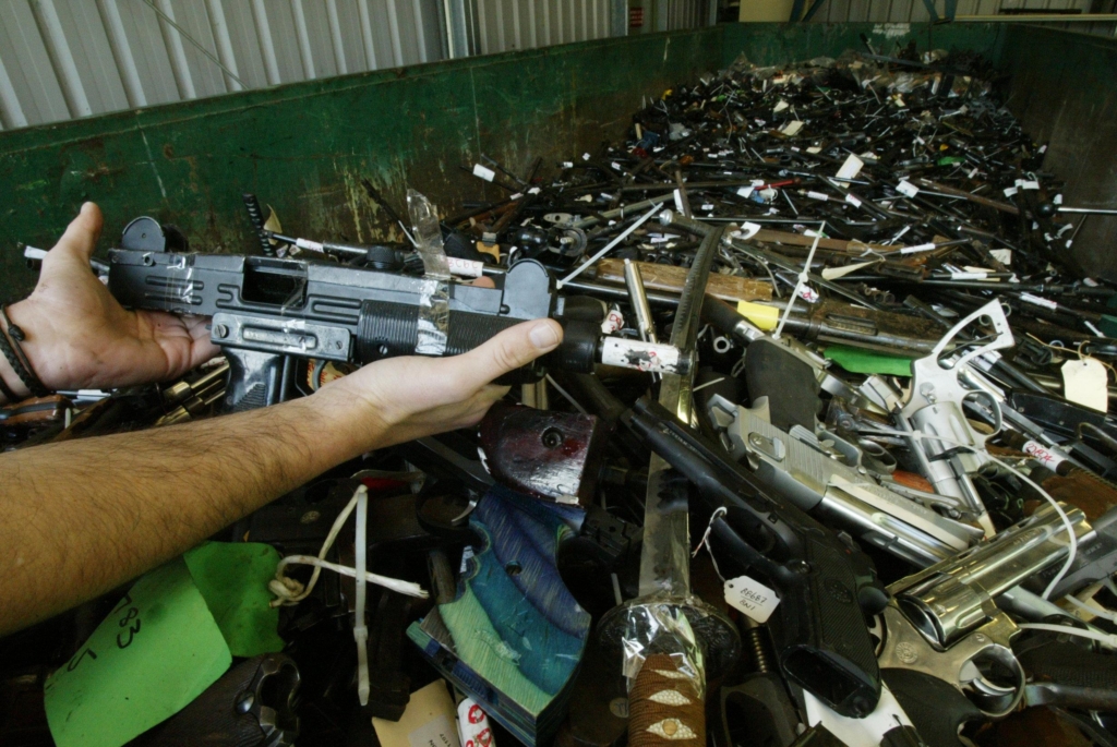 An archive image of a large shipping container that is full of firearms, including pistols and rifles. Someone is holding what appears to be a semi-automatic rifile for the camera. 