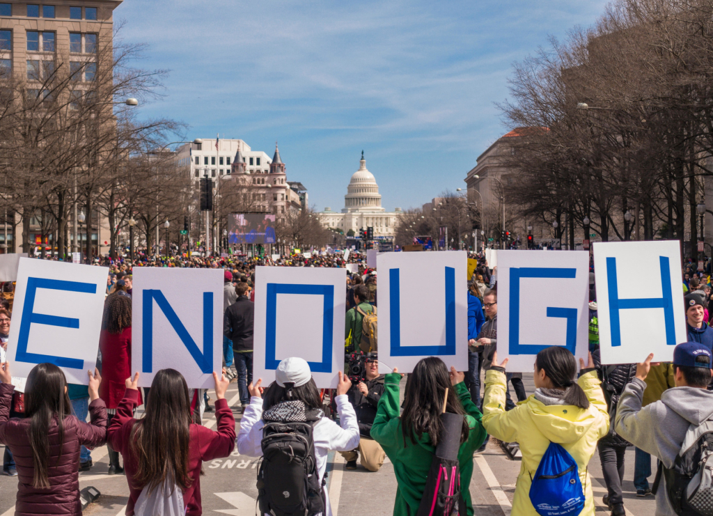 a group of young people march towards the capitol building in washington DC, USA. A group of them are holding signs that read out 'Enough'