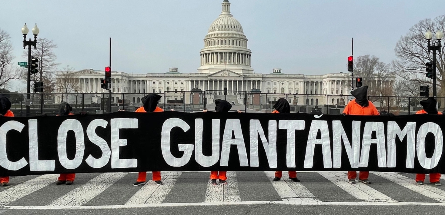 Masked activists wearing orange jumpsuits hold up a sign saying "Close Guantamo" outside the US Capitol building