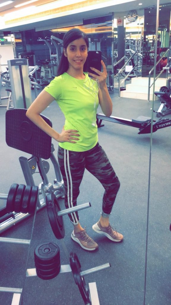 A young woman wearing a yellow top stands in the gym. 