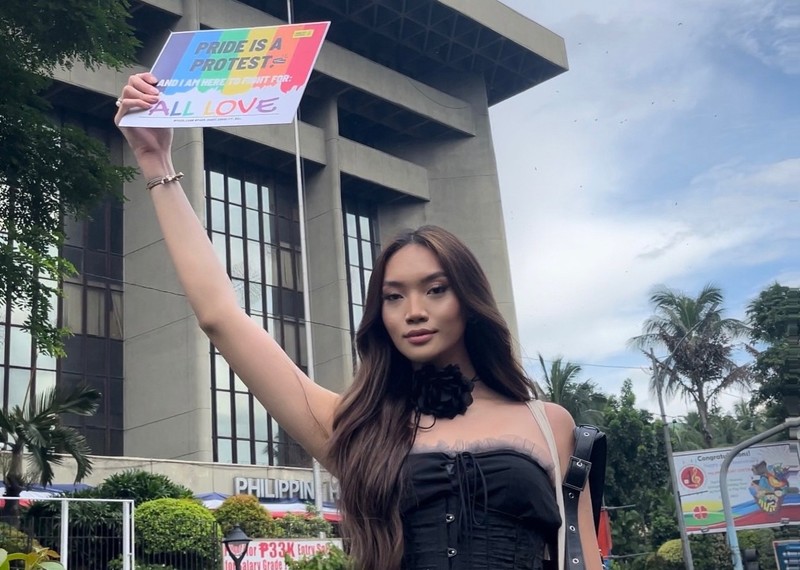 A young woman from the Philippines holds up a Pride sign