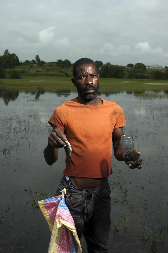 A fisherman showing a small fish and an oil lump collected from a polluted river