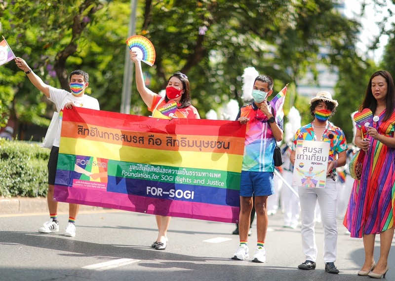 Five activists hold the Pride flag as they walk down the street in Bangkok