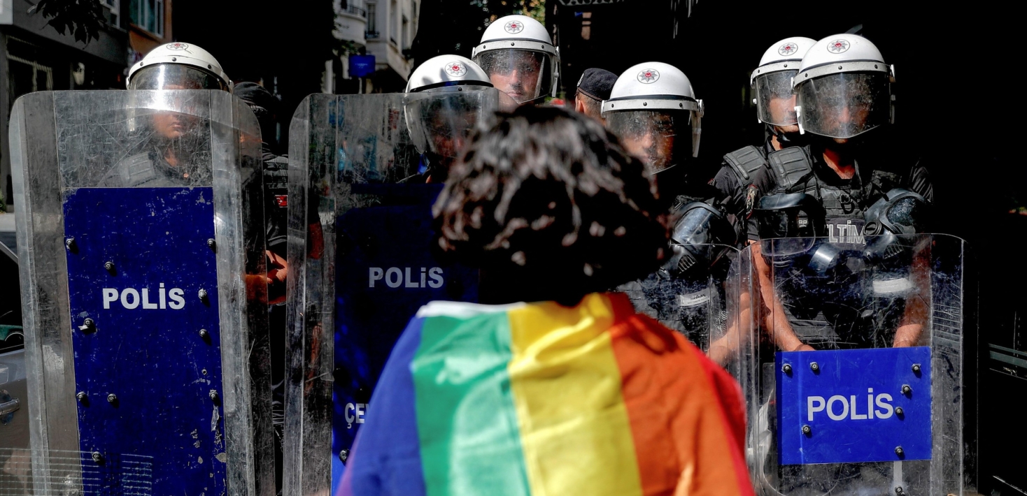 A participant faces riot policemen wearing a rainbow flag during a Pride march in Istanbul.