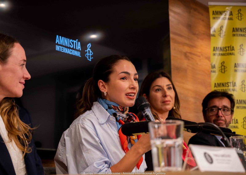 Actress Thelma Fardin, sits on a panel of four and holds a microphone.