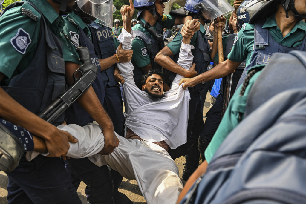 a man is carried away by a group of police. They are grabbing his arms and legs. 