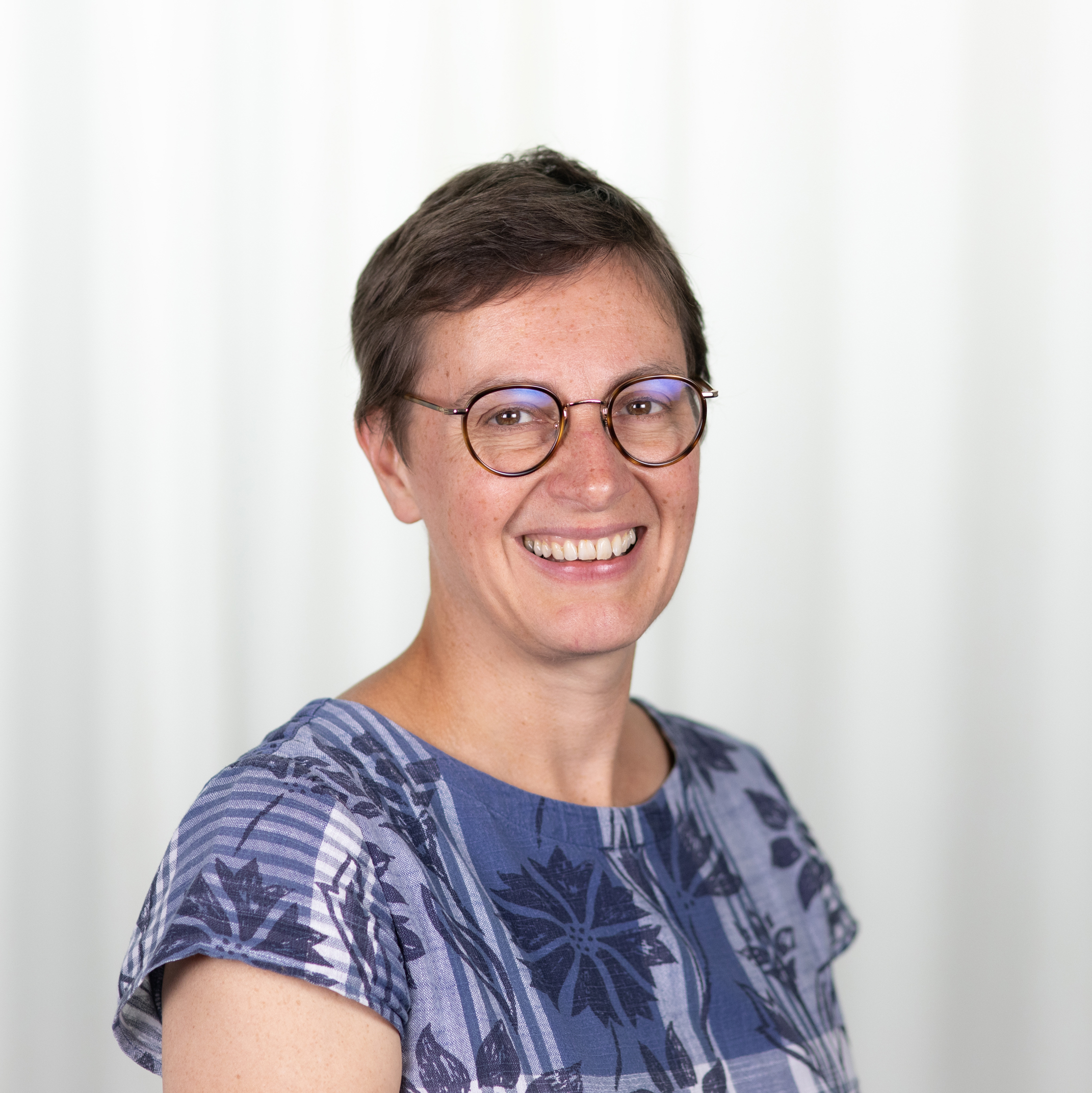 Kathryn is wearing a blue top and glasses and smiling at the camera.