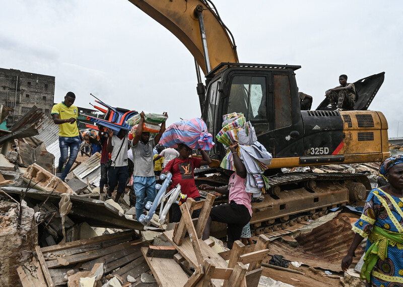 Residents carrying furniture walk past an excavator during the destruction of houses in the district of Boribana in Abidjan during an eviction operation on 23 February 2024