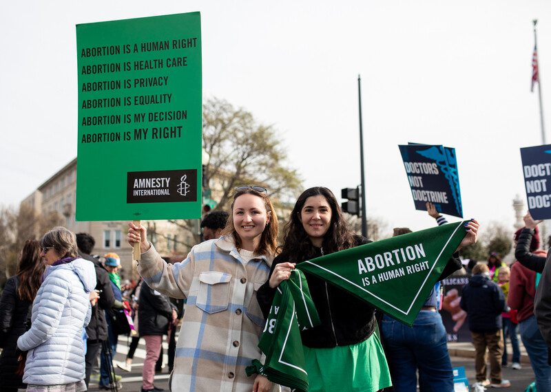 Dos mujeres sostienen sendos soportes verdes en los que se lee que el aborto es un derecho humano.