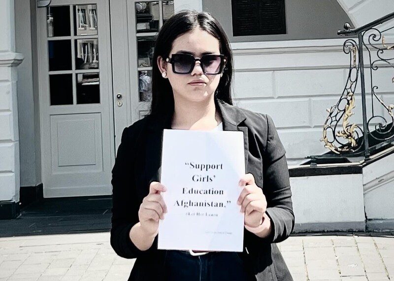 A young woman in sunshades holds up a sign that reads support girls education in Afghanistan