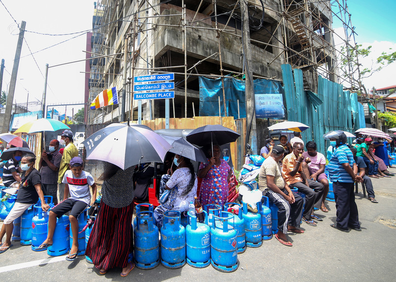 A long line of people waiting in the sun with blue gas canisters.